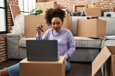 Young african american woman showing keys of new home on video call scared and amazed with open mouth for surprise, disbelief face 