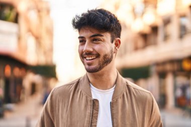 Young hispanic man smiling confident looking to the side at street