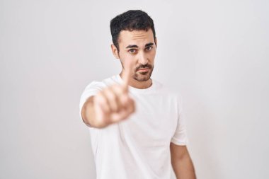 Handsome hispanic man standing over white background pointing with finger up and angry expression, showing no gesture 