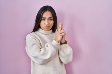 Pembe arka planda duran genç Güney Asyalı kadın sembolik bir silahla el hareketleriyle cinayet silahlarıyla oynuyor, kızgın surat. 