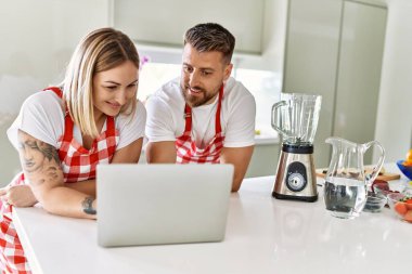 Genç çift dizüstü bilgisayarı kullanarak gülümsüyor. Mutfakta smoothie tarifi kullanıyor.