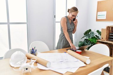 Beyaz kadın gülümsüyor. Mimarlık stüdyosunda çalışan akıllı telefondan konuşuyor.