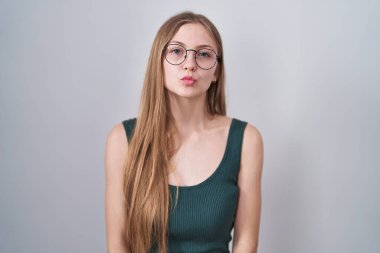 Young caucasian woman standing over white background looking at the camera blowing a kiss on air being lovely and sexy. love expression. 