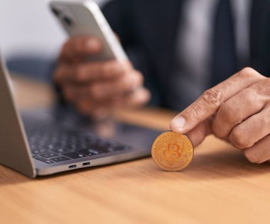 Young bald man using smartphone holding bitcoin at office