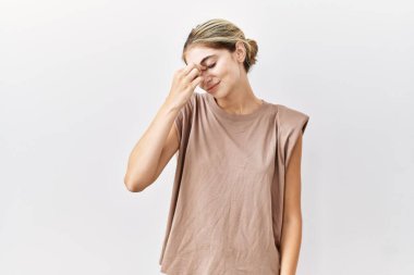 İzole edilmiş arka planda duran genç sarışın kadın yorgun burnu ve gözleri ovuşturup yorgun ve baş ağrısı çekiyor. Stres ve hüsran kavramı. 