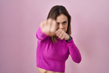 İspanyol kadın pembe arka planda duruyor. Yumruk yumruğa dövüşmek, agresif ve öfkeli saldırı, tehdit ve şiddet. 