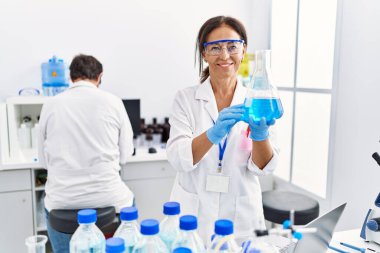 Laboratuvarda deney tüpü tutan bilim adamı üniforması giyen orta yaşlı erkek ve kadın partnerler.