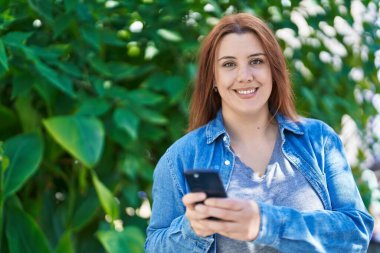 Young beautiful plus size woman smiling confident using smartphone at park