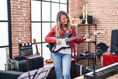 Young woman musician playing electrical guitar at music studio