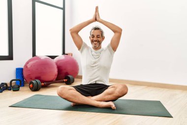 Orta yaşlı, gri saçlı, gülümseyen, spor merkezinde yoga eğitimi alan bir adam.