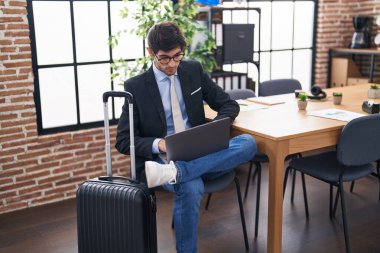 Young hispanic man business worker waiting for travel using laptop at office