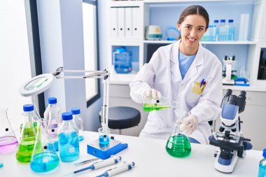 Genç ve güzel İspanyol bilim kadını laboratuarda test tüpüne sıvı döküyor.