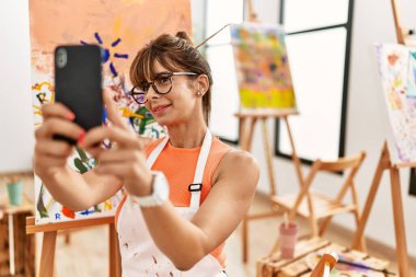 Genç İspanyol kadın gülümsüyor. Sanat stüdyosundaki akıllı telefondan özçekim yapıyor.