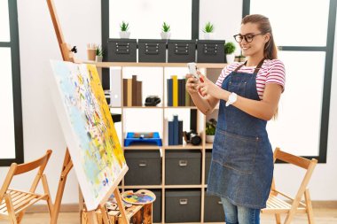 Kendine güvenen genç bir kadın resim stüdyosundaki akıllı telefondan fotoğraf çekiyor.