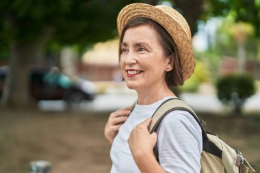 Orta yaşlı bir turist parkta sırt çantası takıp gülümsüyor.
