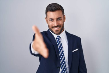 Yakışıklı İspanyol takım elbiseli ve kravatlı adam gülümseyerek dostça tokalaşıyor ve hoş geldin diyor. başarılı iş. 