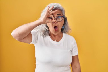 Sarı arka planda duran gri saçlı orta yaşlı kadın şaşırmış yüz ifadesiyle şaşırmış, parmaklarından bakan gözler. İnançsız ifade. 