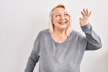 Orta yaşlı beyaz bir kadın beyaz arka planda dans ediyor mutlu ve neşeli, hareketli ve kendinden emin bir şekilde müzik dinliyor. 