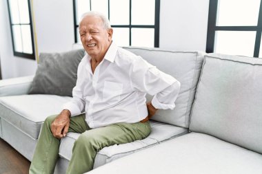 Senior man suffering for backache sitting on sofa at home