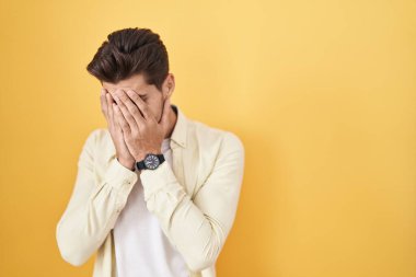Sarı arka planda dikilen genç İspanyol adam. Ağlarken suratını ellerle kapatıyor. depresyon kavramı. 