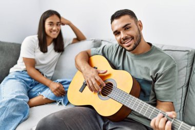 Genç latin çift evdeki kanepede oturup klasik gitar çalıyor..