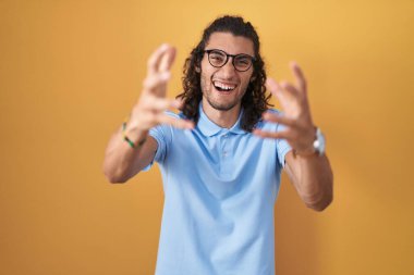 Sarı arka planda dikilen İspanyol genç adam öfkeyle bağırıyor, elleri boğazlamaya çalışıyor, deli gibi bağırıyor. 