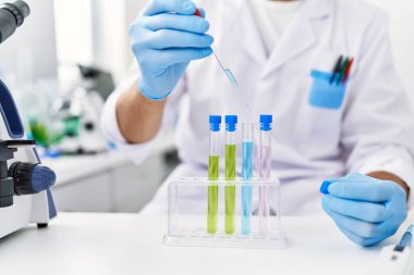 Laboratuvarda pipet ve test tüpü kullanarak bilim adamı üniforması giyen İspanyol genç bir adam.