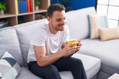 Genç İspanyol adam evdeki kanepede kahve içiyor.