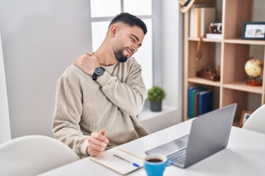 Genç Arap adam sırt ağrısı çekiyor. Masada oturuyor ve evde çalışıyor.