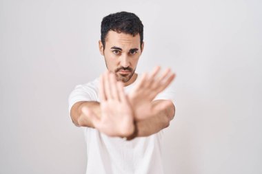 Handsome hispanic man standing over white background rejection expression crossing arms and palms doing negative sign, angry face 