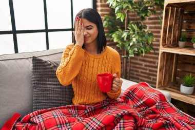 Kanepede oturan genç İspanyol kadın evde kahve içiyor. Yarı yüzünü, göz ve ağzını eliyle kapatmaktan yoruluyor. Yüzüm acıyor.. 