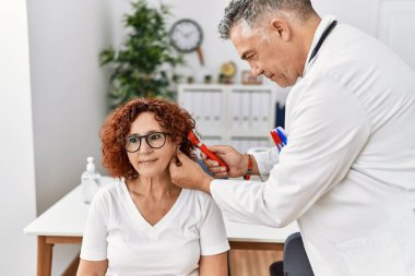Orta yaşlı erkek ve kadın doktor üniforması giyiyorlar. Kulaklarını muayene ediyorlar. Klinikte tıbbi danışmanlık yapıyorlar.