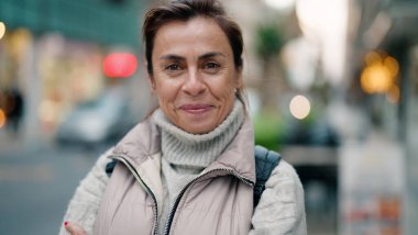 Orta yaşlı İspanyol kadın sokakta kendine güvenerek gülümsüyor.