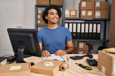 Kıvırcık saçlı İspanyol bir adam küçük işletme ekommersinde çalışıyor. Yüzünde gülümseme, doğal bir ifade ile yan yana bakıyor. Kendinden emin gülen. 