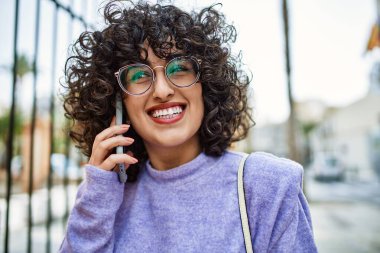 Orta Doğulu genç bir kadın gülümsüyor. Akıllı telefondan konuşuyor.