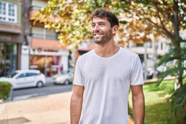 Genç İspanyol adam parkta yürürken kendinden emin gülümsüyor.