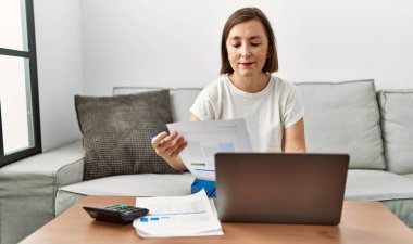 Orta yaşlı İspanyol kadın ev işlerinde ev işleri için dizüstü bilgisayar kullanıyor.