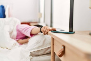 Girl turning off smartphone alarm lying on the bed at bedroom.