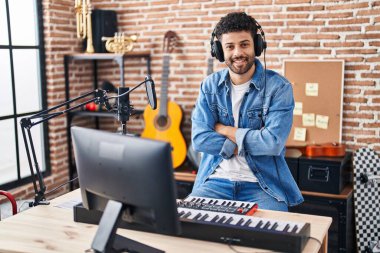 Genç Arap müzisyen, müzik stüdyosunda kollarını kavuşturup gülümsüyor.