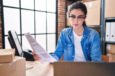 Young beautiful hispanic woman ecommerce using laptop reading document at office