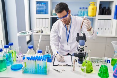 Genç İspanyol bilim adamı laboratuarda test tüpü yazım raporu tutuyor.
