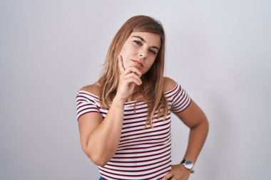 Young hispanic woman standing over isolated background with hand on chin thinking about question, pensive expression. smiling with thoughtful face. doubt concept. 