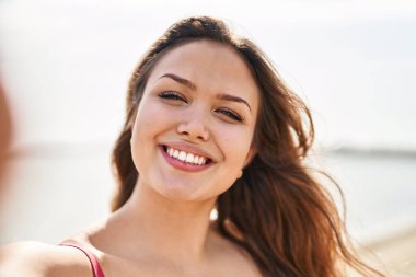Genç ve güzel İspanyol kadın turist gülümsüyor. Kendine güveni tam. Sahilde kamerayla selfie çekiyor.