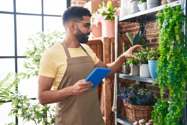 Young arab man florist smiling confident using touchpad at florist