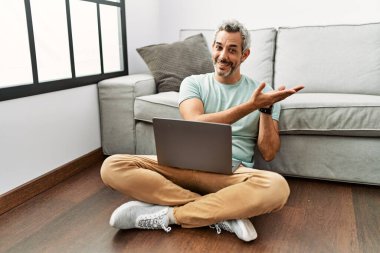 Orta yaşlı İspanyol bir adam oturma odasında dizüstü bilgisayar kullanıyor. Avuçlarını yana açıp fotokopi alanını gösteriyor. Reklam sunuyor. 