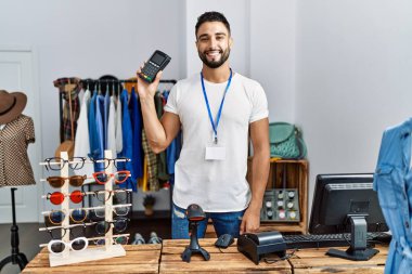 Veri telefonu tutan genç bir Arap esnaf giyim mağazasında çalışıyor.