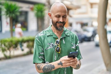 Sokakta akıllı telefon kullanarak kendine güvenen genç kel adam.