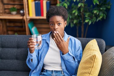 Afrika kökenli Amerikalı bir kadın bir bardak su içerek ağzını eliyle kapadı, şok oldu ve hata yapmaktan korktu. şaşırmış ifade 