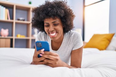 Afrika kökenli Amerikalı bir kadın yatakta akıllı telefon kullanıyor.