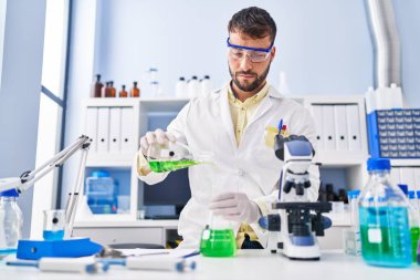 Laboratuvarda sıvı ölçen bilim adamı üniforması giyen İspanyol genç adam.